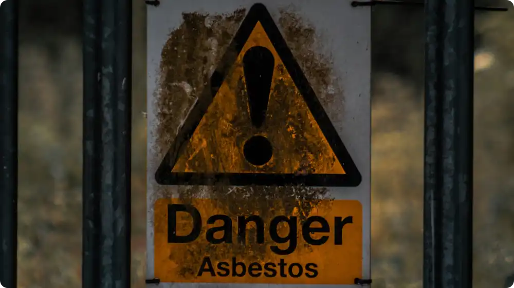 Rusty warning signs on old buildings reading” Danger asbestos” attached to a metal fence at a hazardous site.