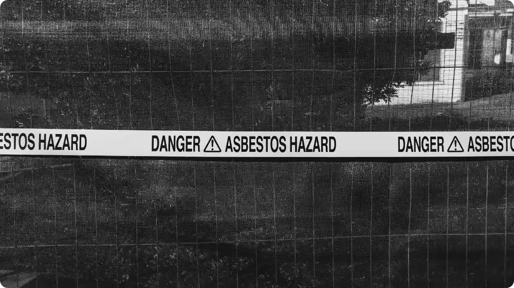 Warning tape marked “Danger Asbestos Hazard” placed on a fence to restrict access to the contaminated area.